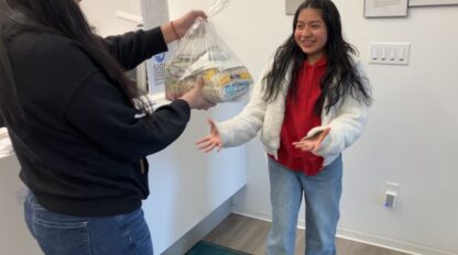 A person hands over a bag of items to a smiling recipient in an indoor setting during a commonpoint challenge.